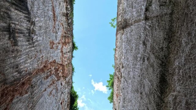 Wide shot of two beautiful cliffs with trees and bushes on top, revealing blue sky and white clouds between them on Bali Island during a clear sunny day.
