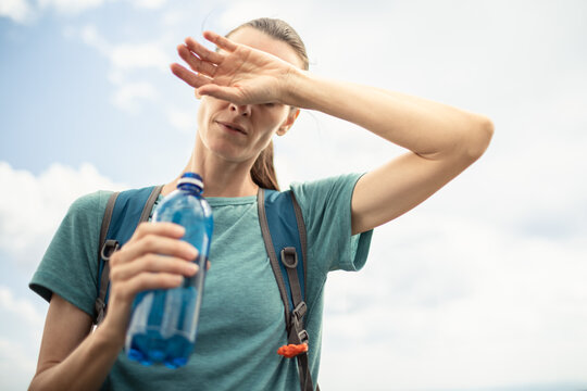 Woman Shielding Eyes From Sun While Holding Drinking Water During Summer Heatwave And Staying Hydrated Outdoors
