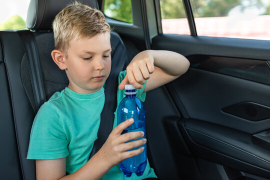 Young Boy Opening Reusable Water Bottle While Sitting In Back Seat Of Car During Summer Family Road Trip
