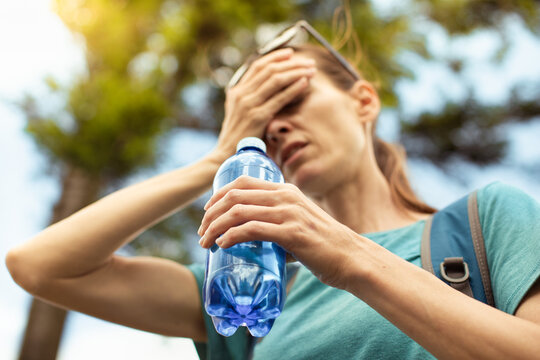 Exhausted Woman Holding Water Bottle And Wiping Forehead During Summer Hike With Heat Stress And Dehydration Concept
