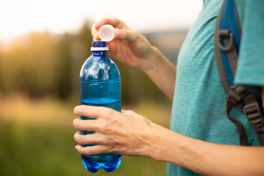 Close Up Of Woman Opening Drinking Water Bottle Before Hiking To Stay Hydrated During Summer Heat
