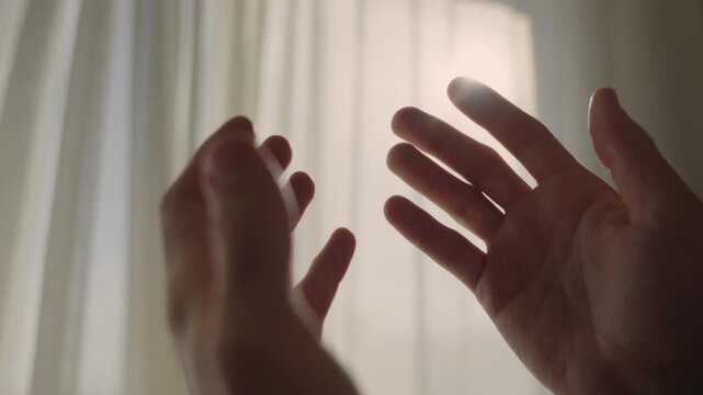 Silhouette of male hands coming together in a prayer gesture against a bright window. Wish or request for god on blessing. Positive emotion religious awakening or enlightenment. Person clasping hands