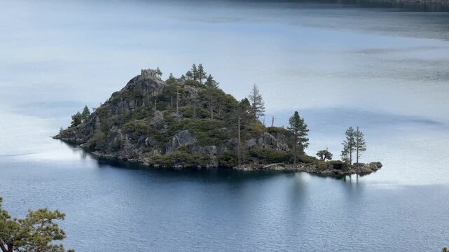 Aerial view of Fannette Island rising from calm blue waters of Emerald Bay near Lake Tahoe with pine trees covering rocky terrain and reflections on the serene lake surface