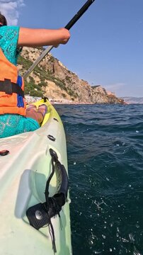 Paddling a kayak along rocky coastlines during summer vacation. Low angle tracking shot.