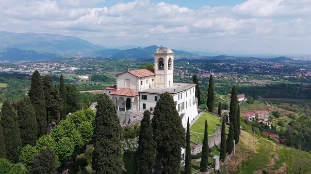 Drone view of historic Sanctuary of Beata Vergine del Carmelo church on green hill overlooking valley in Montevecchia, Italy. Aerial orbiting