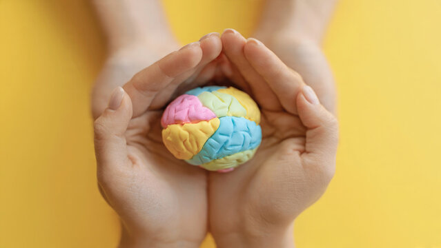 Hands holding a colorful puzzle brain against a bright yellow background representing intelligence and creativity
