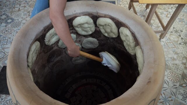 Top view of a baker's hands shaping dough into a hot oven to bake traditional bread in a tundir made of stone. Delicious, aromatic, crispy puris and matnakashi. 
