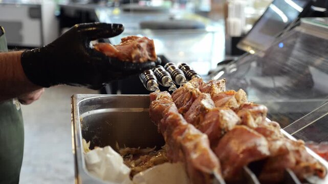 Close-up of a chef wearing gloves stringing marinated pork meat onto a skewer in the kitchen of a restaurant or kebab shop. The process of cooking shish kebab.