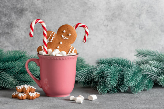 Gingerbread man in a mug with marshmallows and a candy cane, gray background. Christmas symbol. Selective focus.