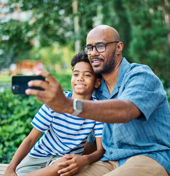 Portrait of father and son having fun using a mobile phone and taking  a selfie photo with camera outdoors in park or nature,, family life, parenting, love and bonding concepts