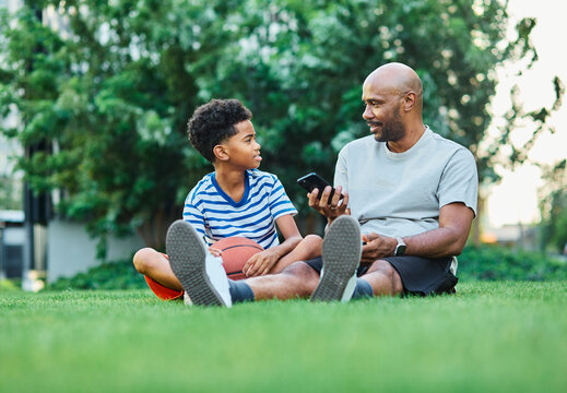 Portrait of father and son having fun using a mobile phone outdoors in park or nature,, family life, parenting, love and bonding concepts