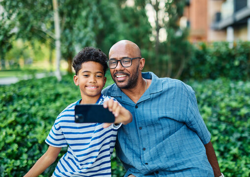 Portrait of father and son having fun using a mobile phone and taking  a selfie photo with camera outdoors in park or nature,, family life, parenting, love and bonding concepts