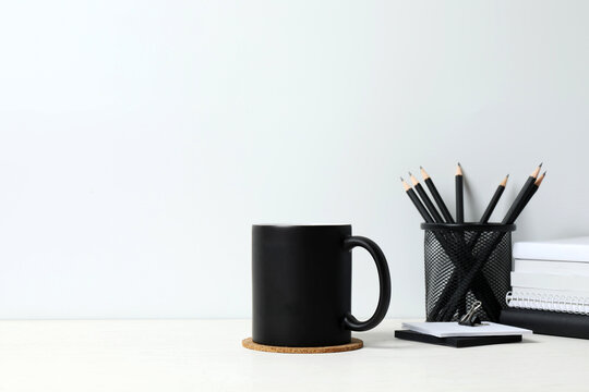 Stylish workspace with wooden desk, office supplies and black cup near the wall, space for text