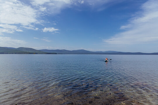 A full man on a sape on a lake among hills with a bright blue sky, calm waters, and a rocky shore, a summer vacation in nature