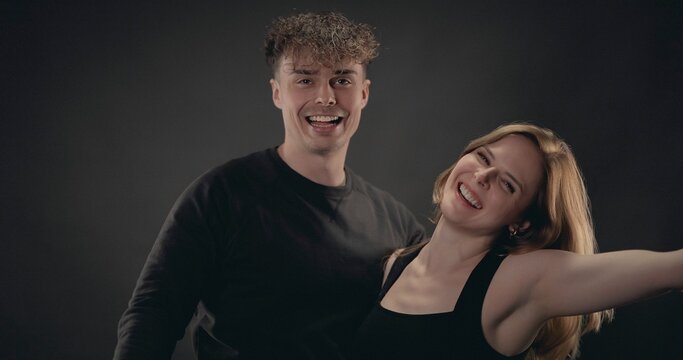 Happy young couple smiling and laughing together against a dark studio background