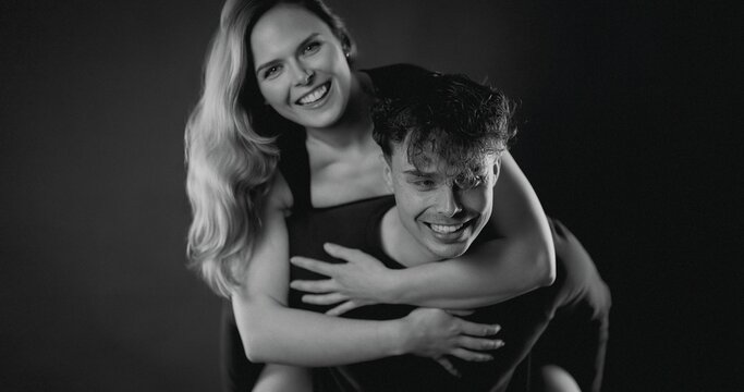 Couple laughing and smiling, sharing joy on a piggyback ride against dark background
