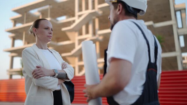 Professional architect and construction foreman discussing building blueprints with a female client at an active construction site. Project planning, teamwork and residential development concept
