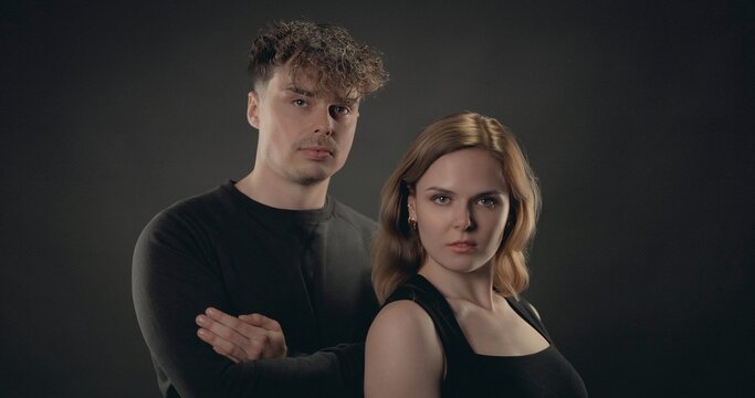Young man and woman posing together in a studio, looking at camera with serious expressions
