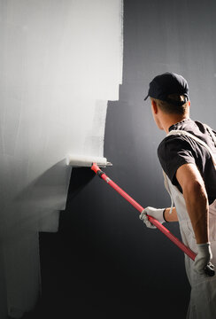 Professional painter painting wall white with long roller during home renovation