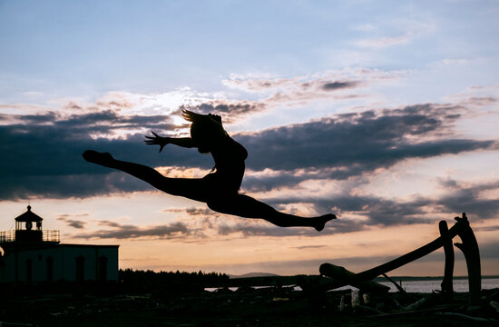 A woman performs a split leap silhouette on a beach