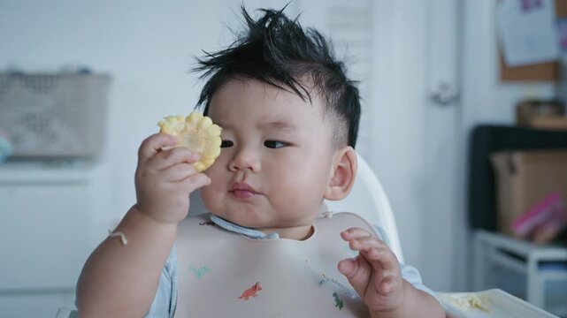 Asian baby boy self feeding sweet corn using baby led weaning method at home.