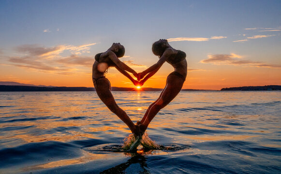 Two women performing partner acrobatics yoga at sunset on water