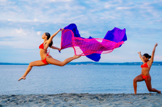 Two women performing partner acrobatics with a scarf on a beach