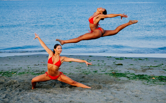 Two women performing partner yoga acrobatics on a beach in wa USA