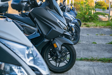 Fototapeta premium Row of parked modern scooters showcasing sleek design lines and contemporary styling in an outdoor urban setting with greenery background.