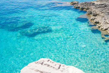 Clear turquoise water near rocky shoreline. Sunlight reflects on the surface, creating a serene coastal scene. Ideal for travel and nature themes. © Mila
