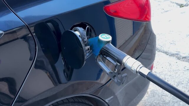 Fuel nozzle with green 92 label in a black car tank at a gas station, closeup view, car refueling, fuel price, petrol economy, road transport.