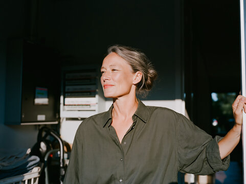 Candid Portrait of Smiling Caucasian Woman in Dark room with cleaning tools with Natural Light