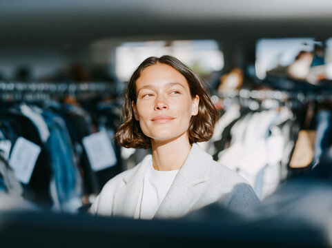 Young Woman Browsing Clothes on Rack in Bright Fashion Vintage Store