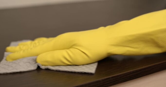 Home cleaning process, dust wiped off the cabinet, hand in yellow gloves cleaning the cabinet with a cloth.