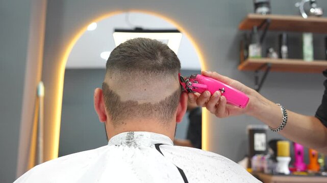 Professional hairdresser creating a fade hairstyle for a man with an electric clipper in a salon