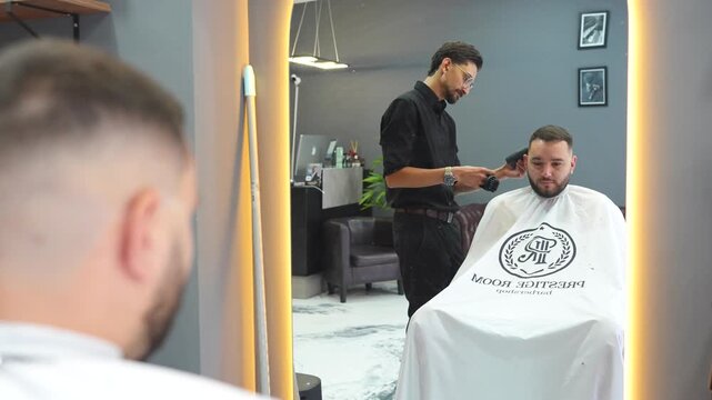 Hair stylist giving a haircut to a male client in a modern barbershop with a hair clipper