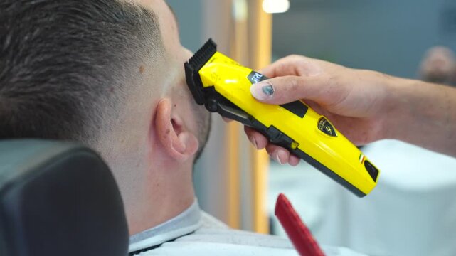 Hairdresser giving a haircut to a male client in a modern barbershop with an electric razor