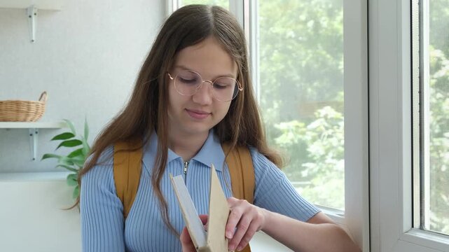 Smiling teen student girl with backpack reading book.Female teenager in glasses doing homework. Education and back to school concept