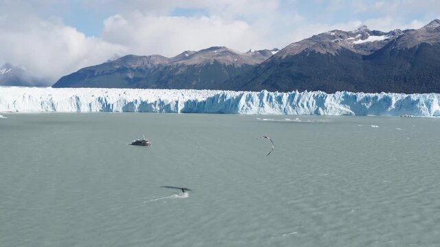 Drone tracks a kitesurfer across Lago Argentino near Perito Moreno Glacier, El Calafate, Santa Cruz, Argentina, with a support boat navigating nearby beneath the glacier front, drone tracking, high ob