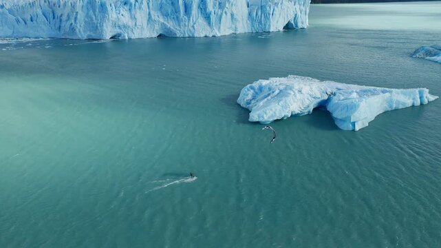 Drone tracks a kitesurfer riding beside a floating iceberg on Lago Argentino near Perito Moreno Glacier, El Calafate, Santa Cruz, Argentina, drone tracking, high oblique aerial view.