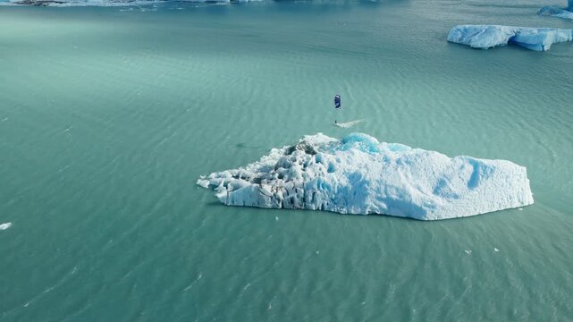 Drone pulls back while tracking a kitesurfer riding beside a massive floating iceberg on Lago Argentino near Perito Moreno Glacier, El Calafate, Santa Cruz, Argentina, drone pullback tracking, high ob