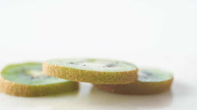 Fresh green kiwi slices falling slow motion isolated