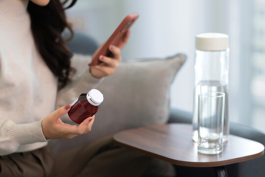 Asian woman holding drug bottle reading information on smartphone at home