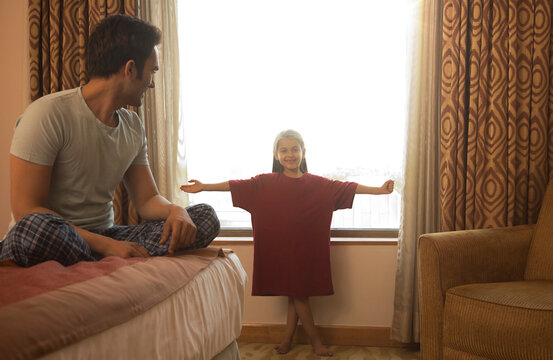 Father watching daughter try on his t-shirt in bedroom