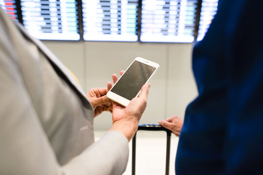 Two people at an airport checking a smartphone near flight boards.