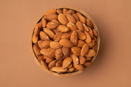 Almond kernels in wooden bowl, whole nuts arranged on brown background with generous copy space. Almond imagery supports healthy food marketing, nutrition content, packaging and lifestyle design.