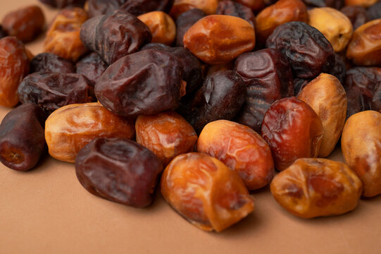 Dried dates scattered on brown background, mixed dark and golden fruit varieties create natural texture and color. Dates support healthy snack marketing, food packaging and nutrition content.