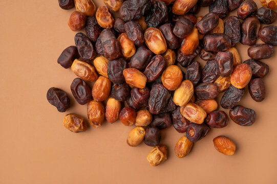 Dried dates scattered on brown background, mixed dark and golden fruit varieties create natural texture and color. Dates support healthy snack marketing, food packaging and nutrition content.