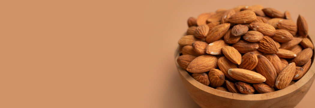 Healthy almonds in wooden bowl, natural nuts displayed from top view on warm brown background with open copy space. Healthy food concept suits nutrition campaigns, wellness content and advertising.