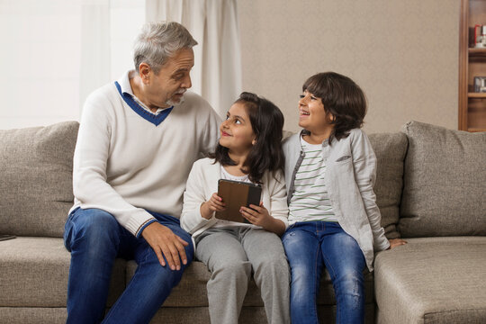 Happy grandfather sitting with grandchildren on sofa